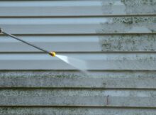 A homeowner uses a pressure washer to cleanse the siding of his house from dirt, mold, and mildew for a fresh appearance.