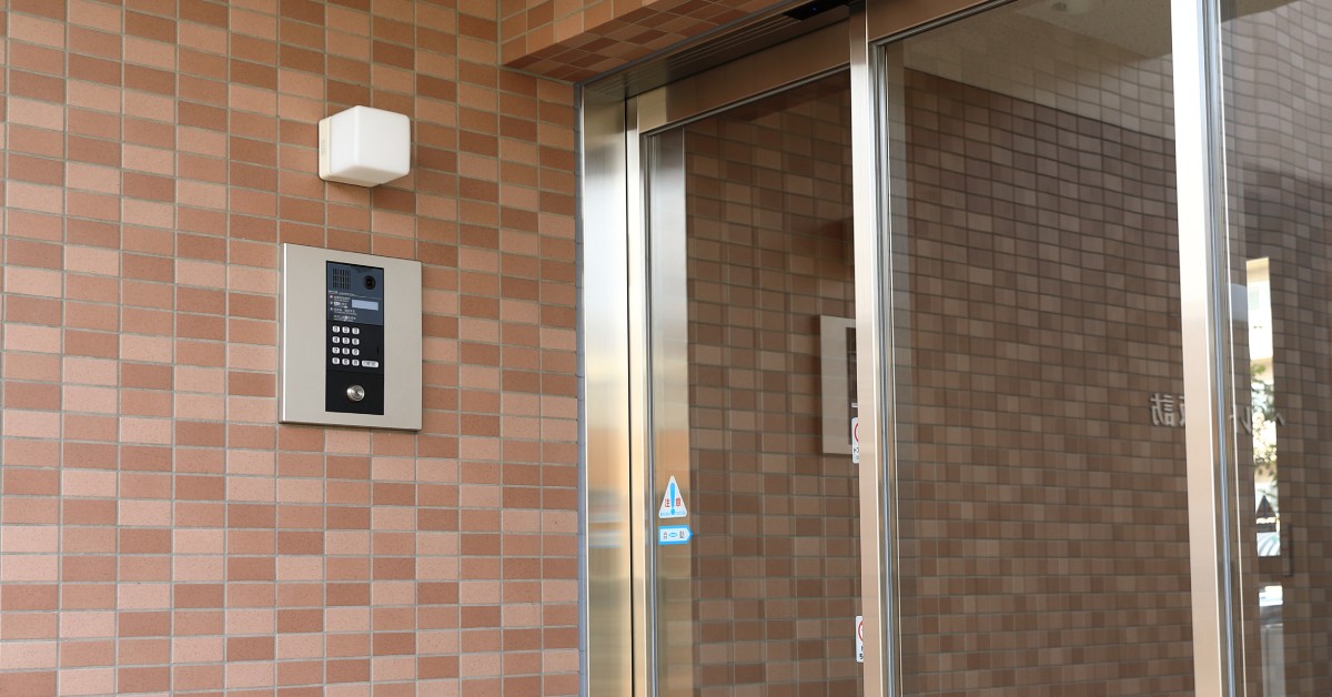 The exterior of a clean and secure residential building. There is an exterior light over an intercom panel outside the door.