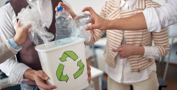 An employee is holding a recycling bin, and other employees are putting empty plastic bottles and bags in it.