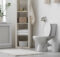 A white toilet and vertical storage unit appear against the bathroom wall. There's a white rug on the tile floor.