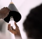 A woman holds the edge of an overhead pendant light fixture as she prepares to install a new LED light bulb.