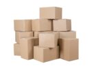 A large stack of plain cardboard boxes sits against a stark white background. The tape keeps the boxes closed.