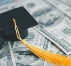 A pile of cash laying on a table with a collegiate graduation cap sitting on top of the cash. There is $100 bills.